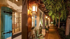 A pathway leading to a building with blue shutters, a stone wall, and a parked car. - Old Ranch Inn - Adults Only  (Palm Springs)
