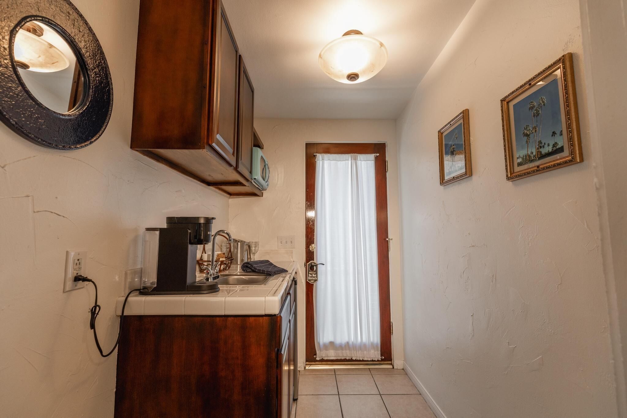 A narrow hallway with a coffee machine, a mirror, and two framed pictures on the wall.