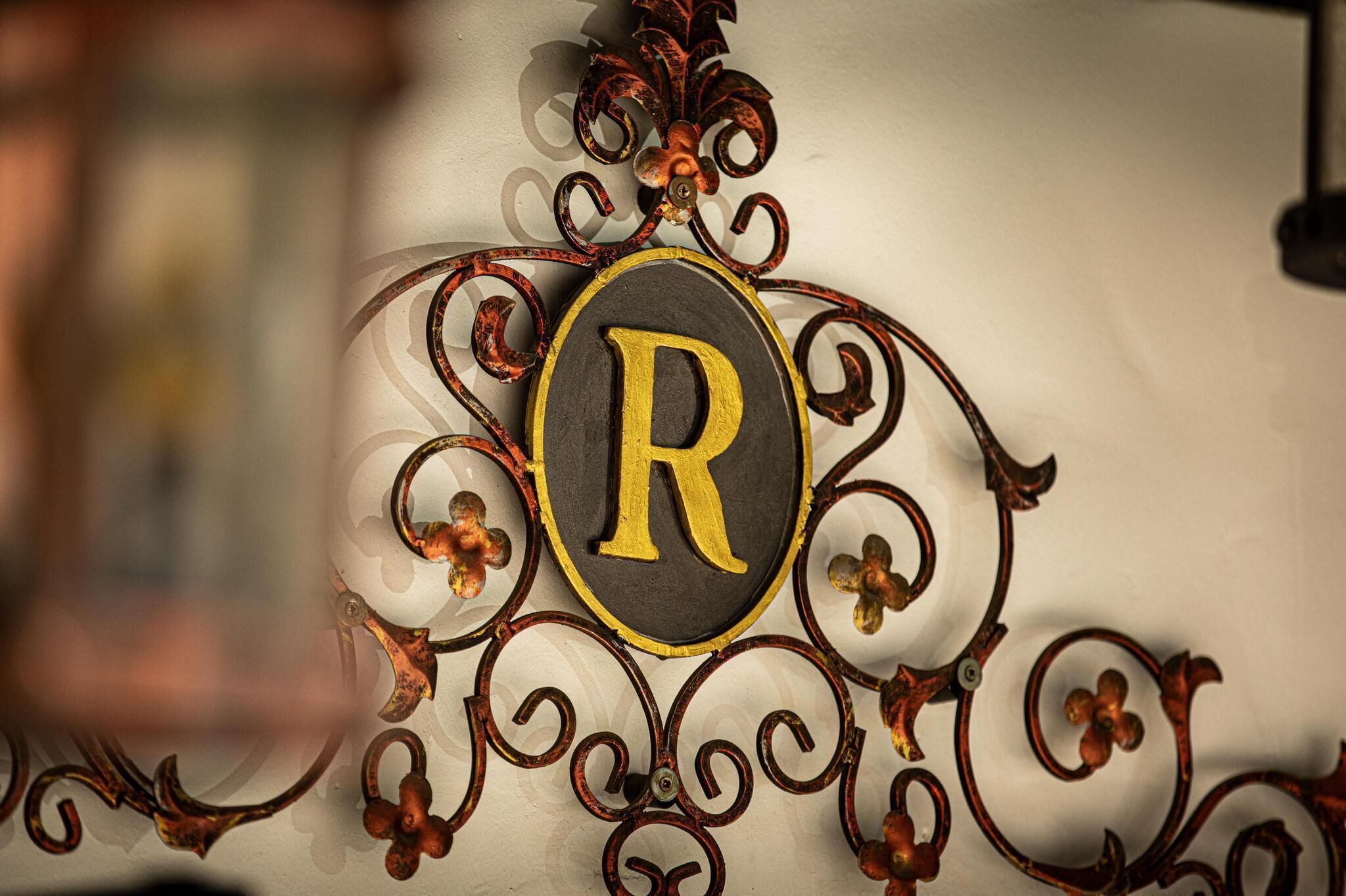 A decorative metal sign with a large 'R' in the center, surrounded by ornate metalwork.