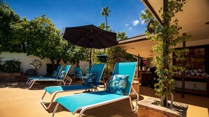 A poolside area with lounge chairs and an umbrella, surrounded by greenery and a building with a visible sign. - Old Ranch Inn - Adults Only  (Palm Springs)