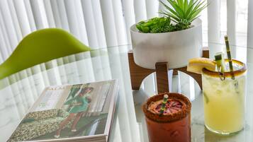 Un magazine sur une table, une boisson décorée d’une garniture et une plante dans un pot blanc.