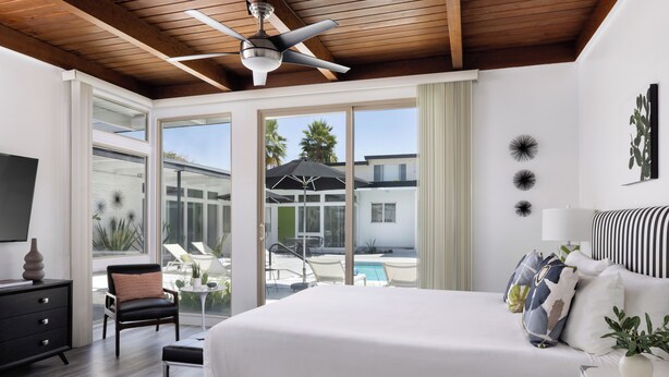 A modern bedroom with a large bed, a ceiling fan, and a view of the outdoor pool area. - The Three Fifty Hotel (Palm Springs)