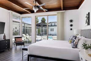 A modern bedroom with a large bed, a ceiling fan, and a view of the outdoor pool area.