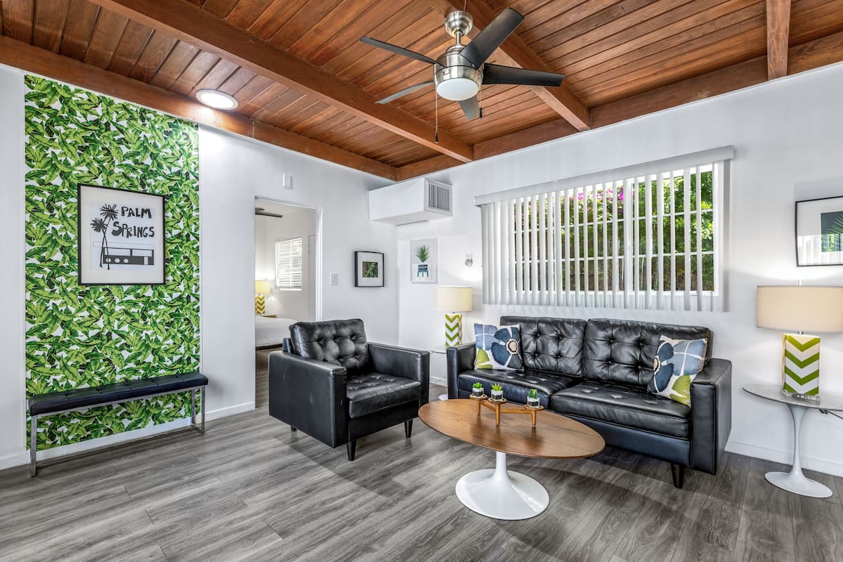 A modern living room with a black leather sofa, a round coffee table, and a ceiling fan.