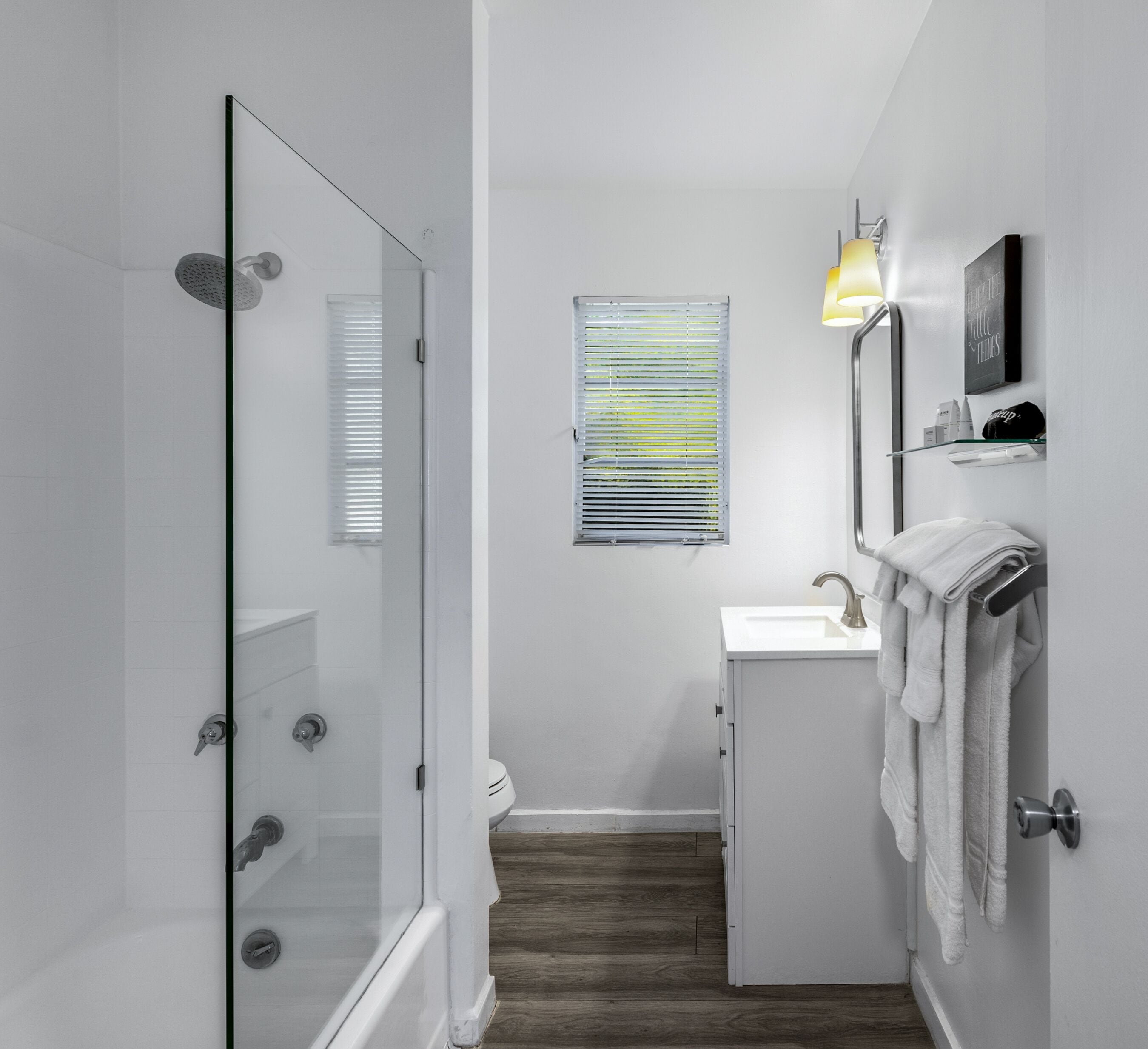 Un baño moderno con cabina de ducha de vidrio, un lavabo pequeño y una ventana con persianas.