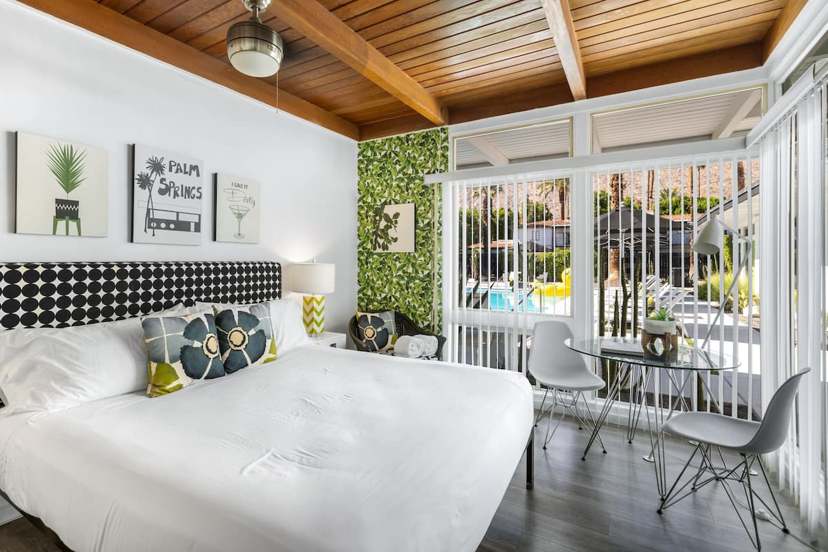 A bedroom with a large bed, a view of a pool, and a balcony with chairs.