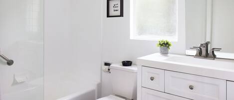 Et moderne badeværelse med brusekabine i glas, et hvidt toilet, en vask med spejl og en lille potteplante på bordet.