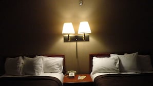 A hotel room with two beds, each with white bedding and a wooden headboard. There is a nightstand between the beds with a lamp and a telephone. - Bangor Inn & Suites (Bangor)