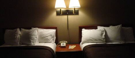 A hotel room with two beds, each with white bedding and a wooden headboard. There is a nightstand between the beds with a lamp and a telephone.