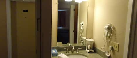 Un baño de hotel con lavamanos, espejo, secador de pelo y cafetera.