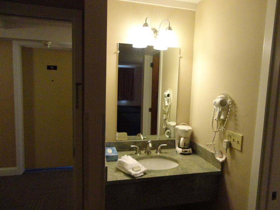 A hotel bathroom with a sink, mirror, hairdryer, and a coffee maker.