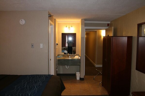 Une chambre d’hôtel comprenant un lit, une salle de bain avec un lavabo et un miroir, et une armoire en bois.