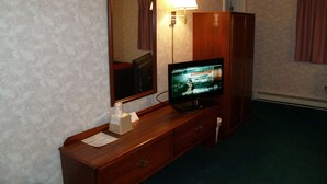 A hotel room with a wooden dresser, a television, a mirror, and a lamp. - Bangor Inn & Suites (Bangor)