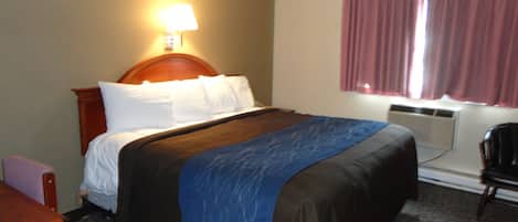A hotel room with a bed, a desk, a lamp, and a window with curtains.