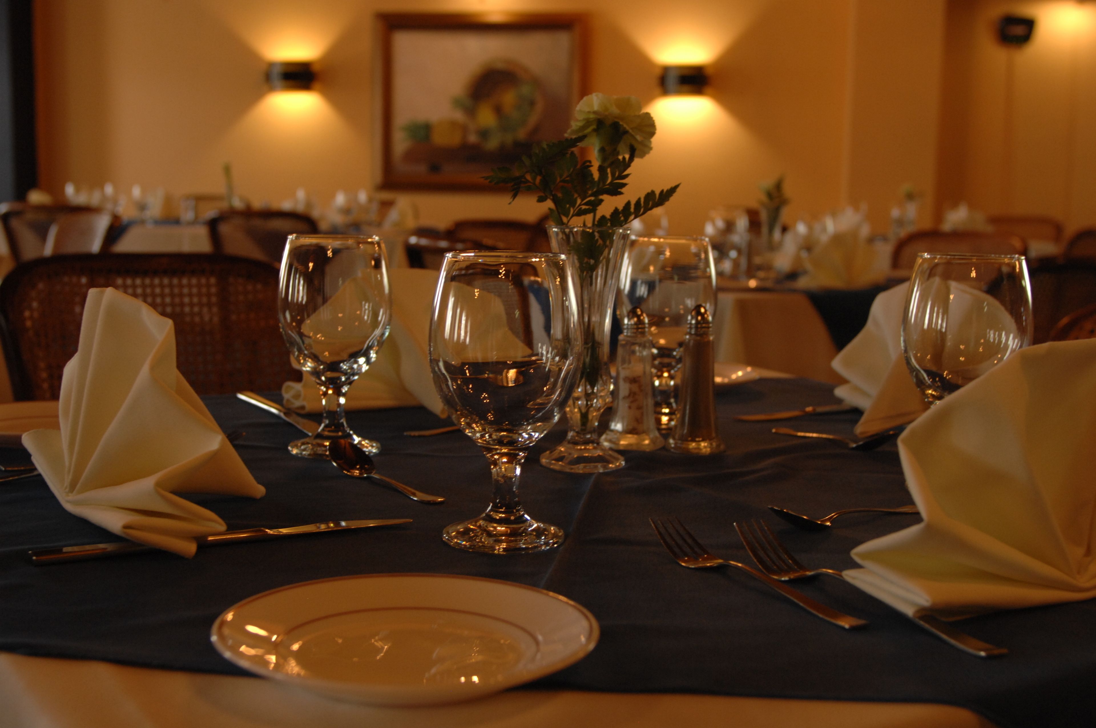 A dining table set with plates, glasses, and cutlery, with a vase of flowers in the center.