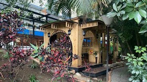 Una estructura de madera con porche cubierto, rodeada por un jardín con diversas plantas y un camino de grava.