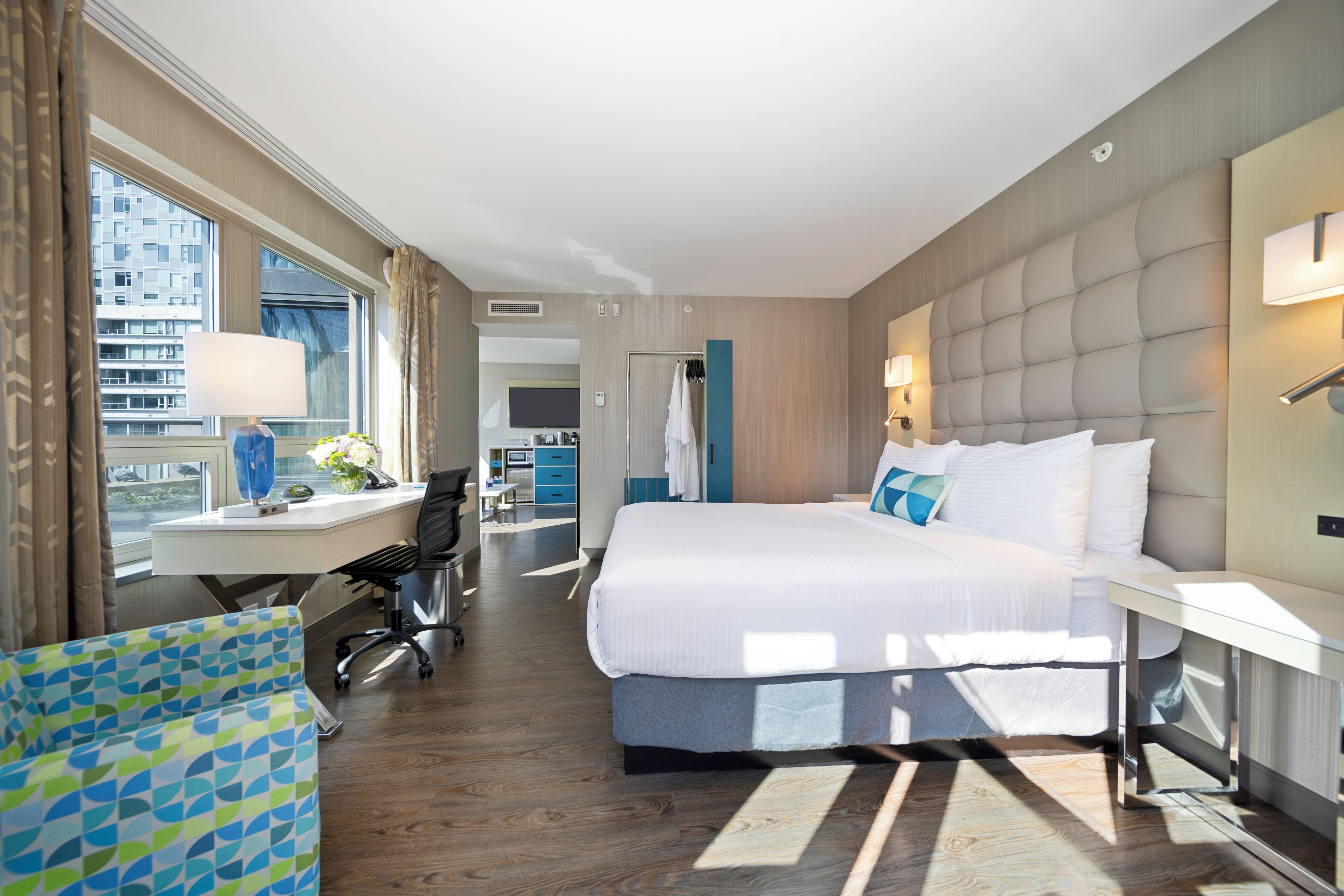 A hotel room with a large bed, a desk with a chair, a view of the city, and a bathroom with a shower and toilet.