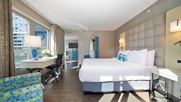 A hotel room with a large bed, a desk with a chair, a view of the city, and a bathroom with a shower and toilet.