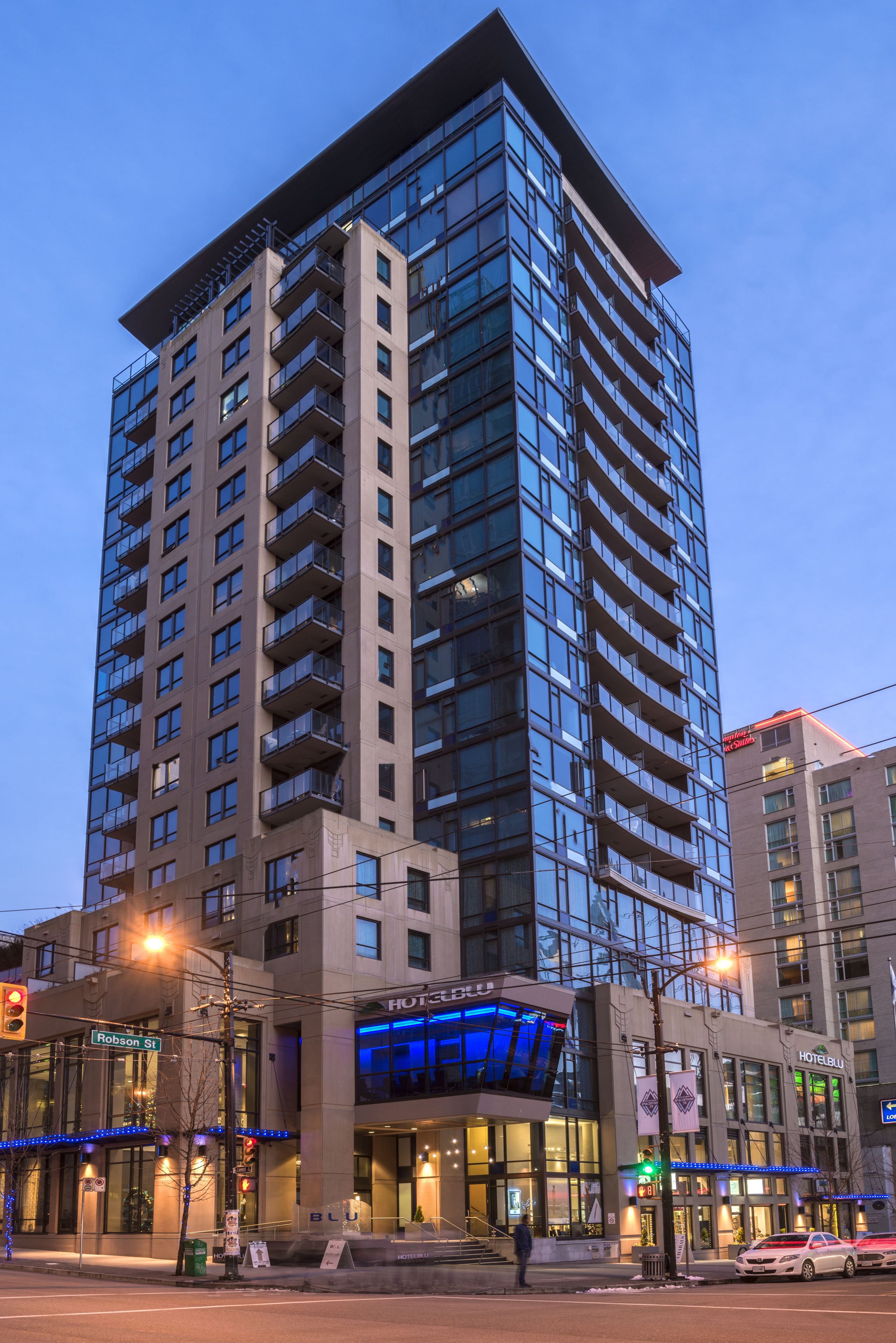 A high-rise hotel with multiple balconies, a modern glass facade, and a visible entrance with illuminated signage.