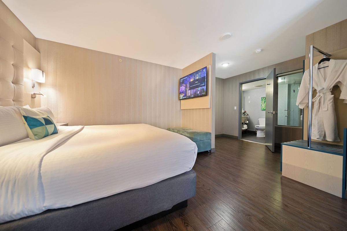 A modern hotel room with a large bed, a flat-screen TV, a seating area, and a visible bathroom.