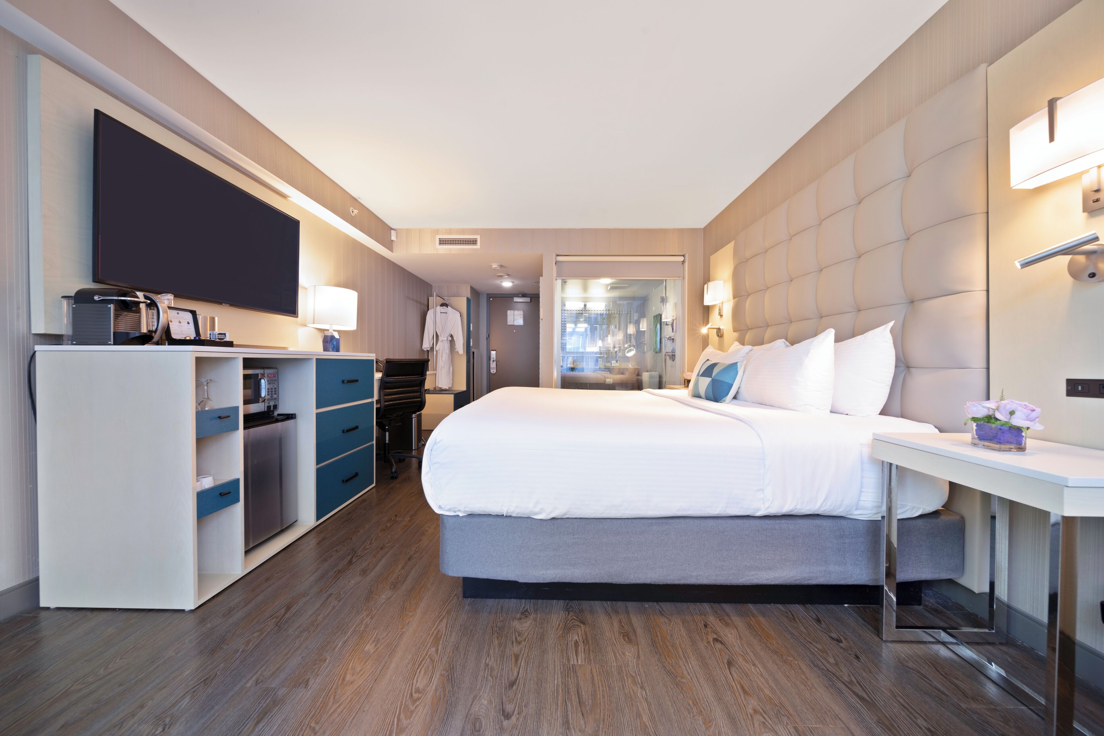 A modern hotel room with a large bed, a flat-screen TV, a desk with a lamp, and a wardrobe.