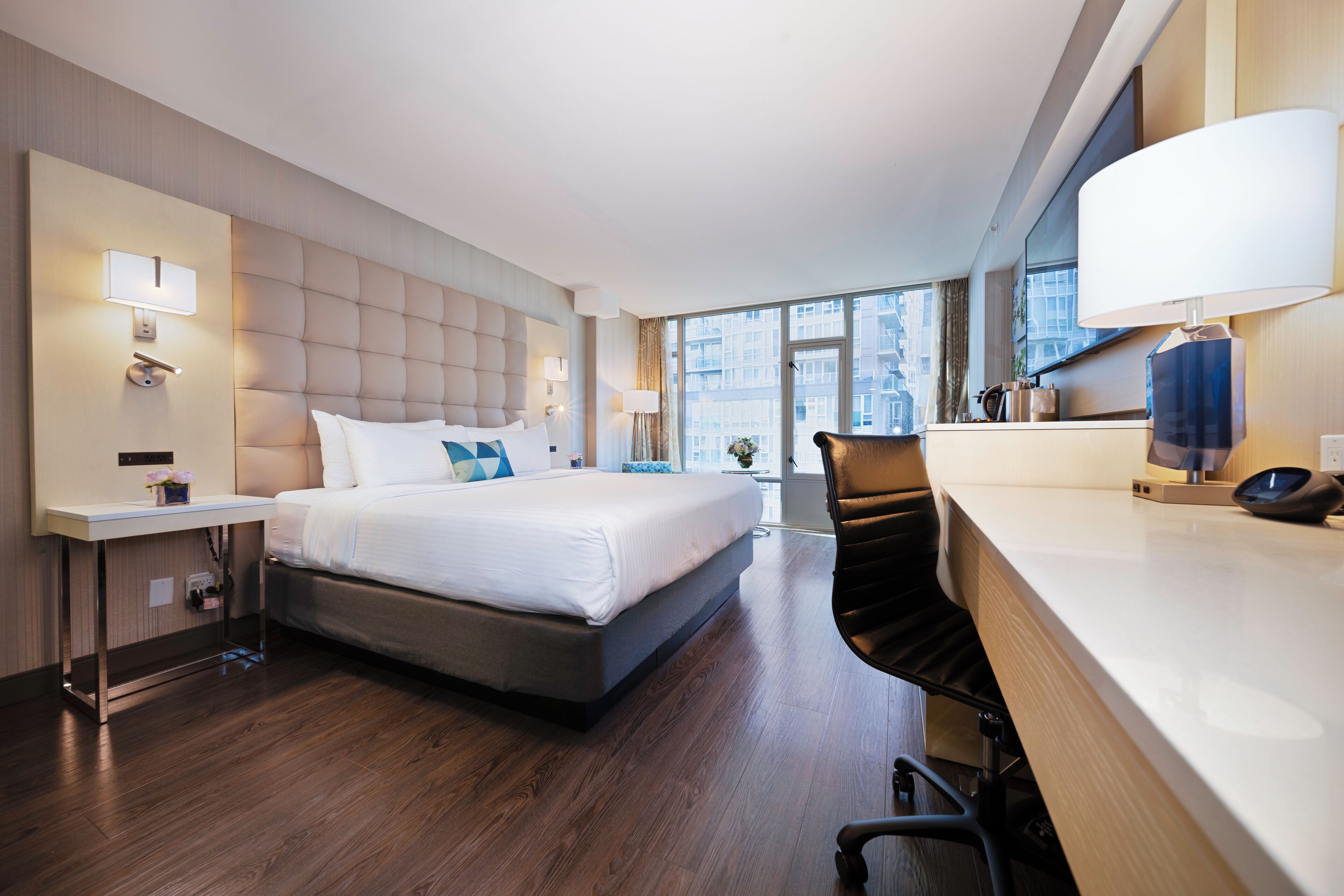 A modern hotel room with a large bed, bedside tables, a desk, and a chair.
