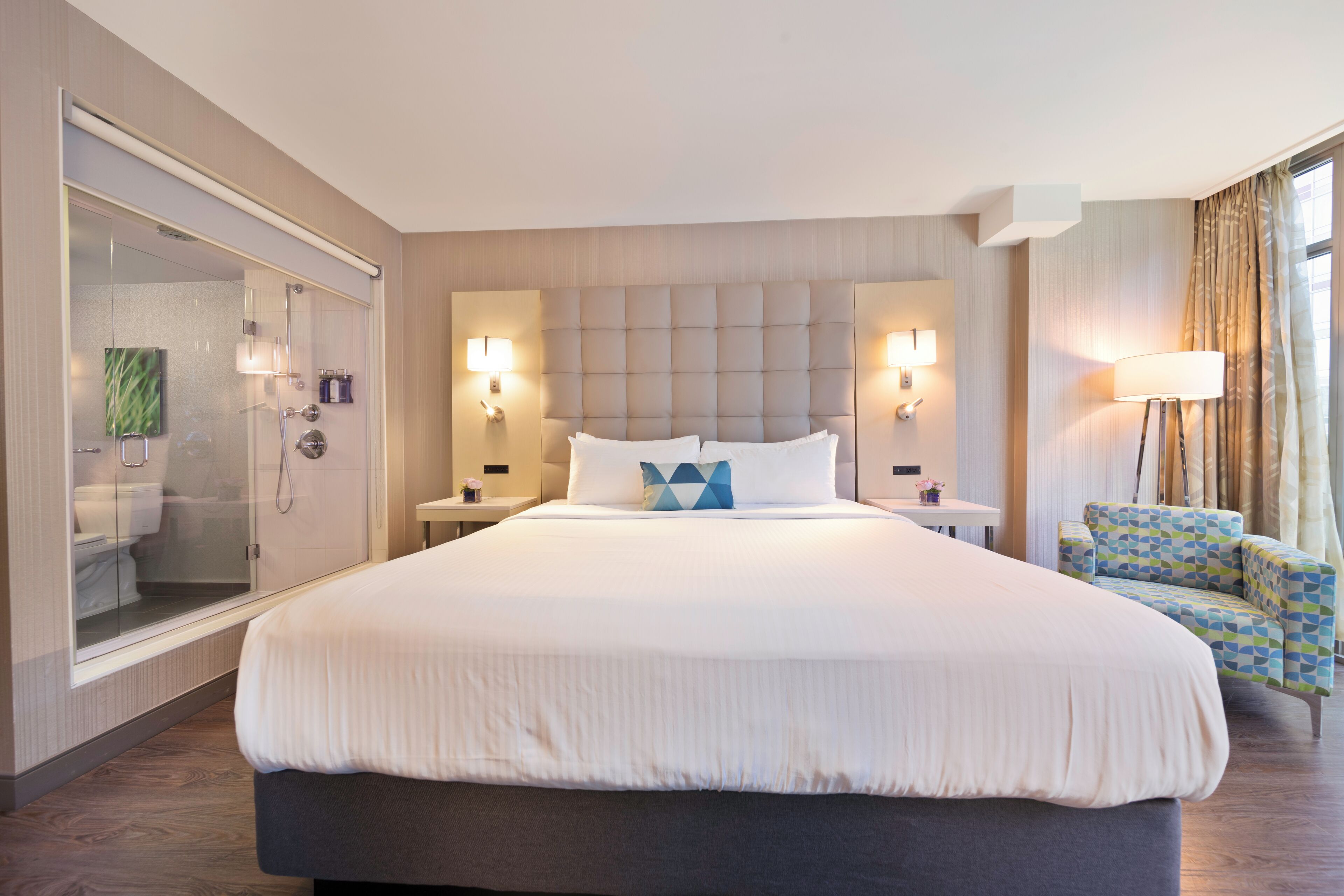 Une chambre d’hôtel moderne dotée d’un grand lit, d’une douche en verre et d’un coin salon avec un fauteuil.