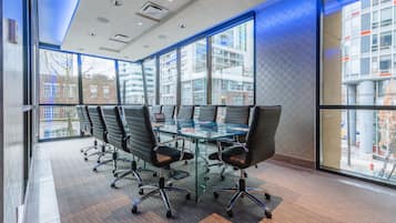 A conference room with a glass table and black chairs, large windows, and a view of buildings.