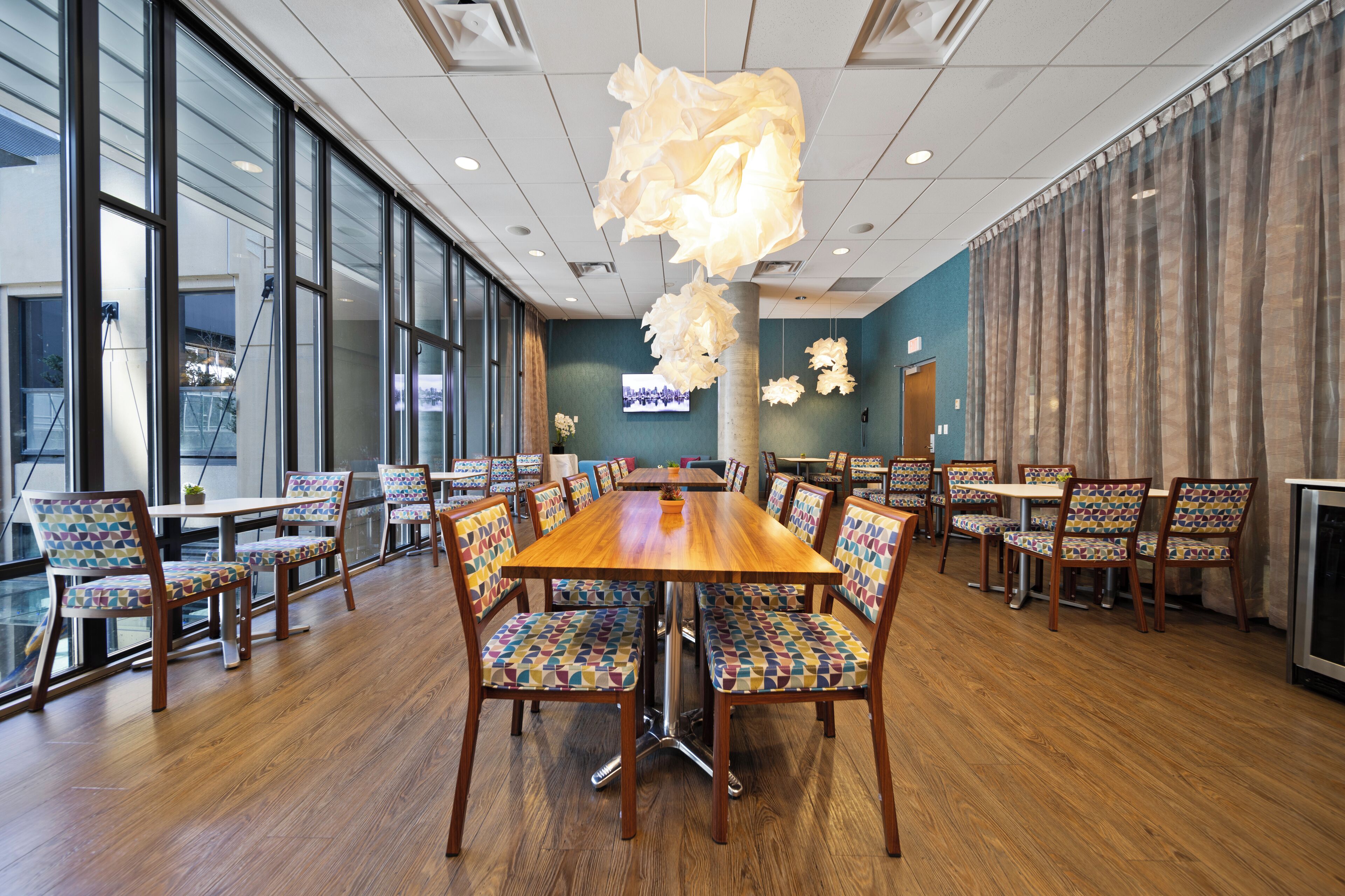 A spacious dining area with a large wooden table surrounded by colorful chairs, large windows, and a modern ceiling design.