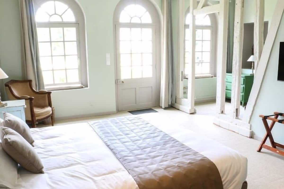Une chambre à coucher avec un lit, deux fenêtres, une chaise et un miroir.