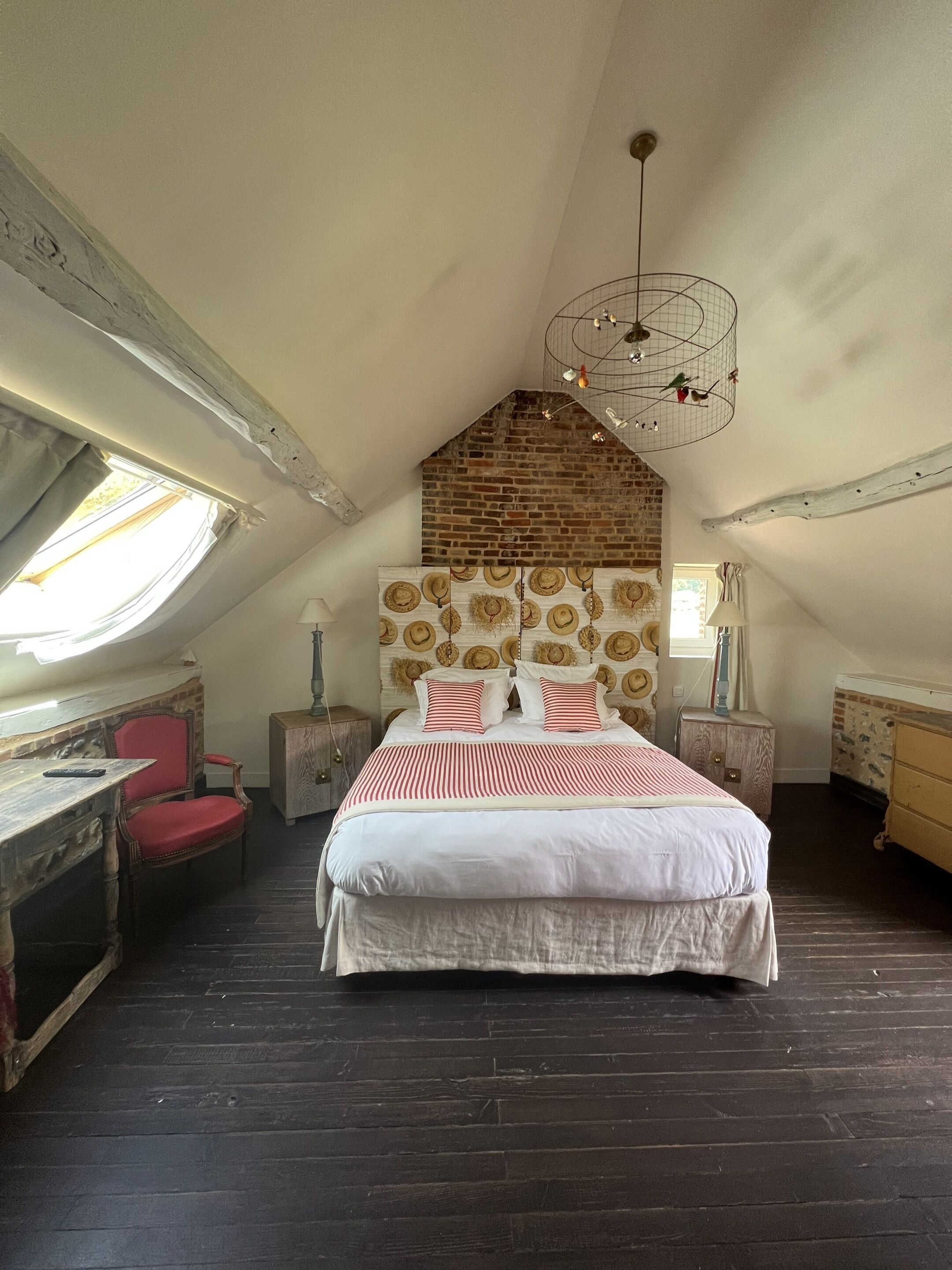 Ein Schlafzimmer mit schrägverdeckter Decke, einem Bett mit gestreifter Bettwäsche, einer rustikalen Ziegelwand und einer hängenden Leuchte.