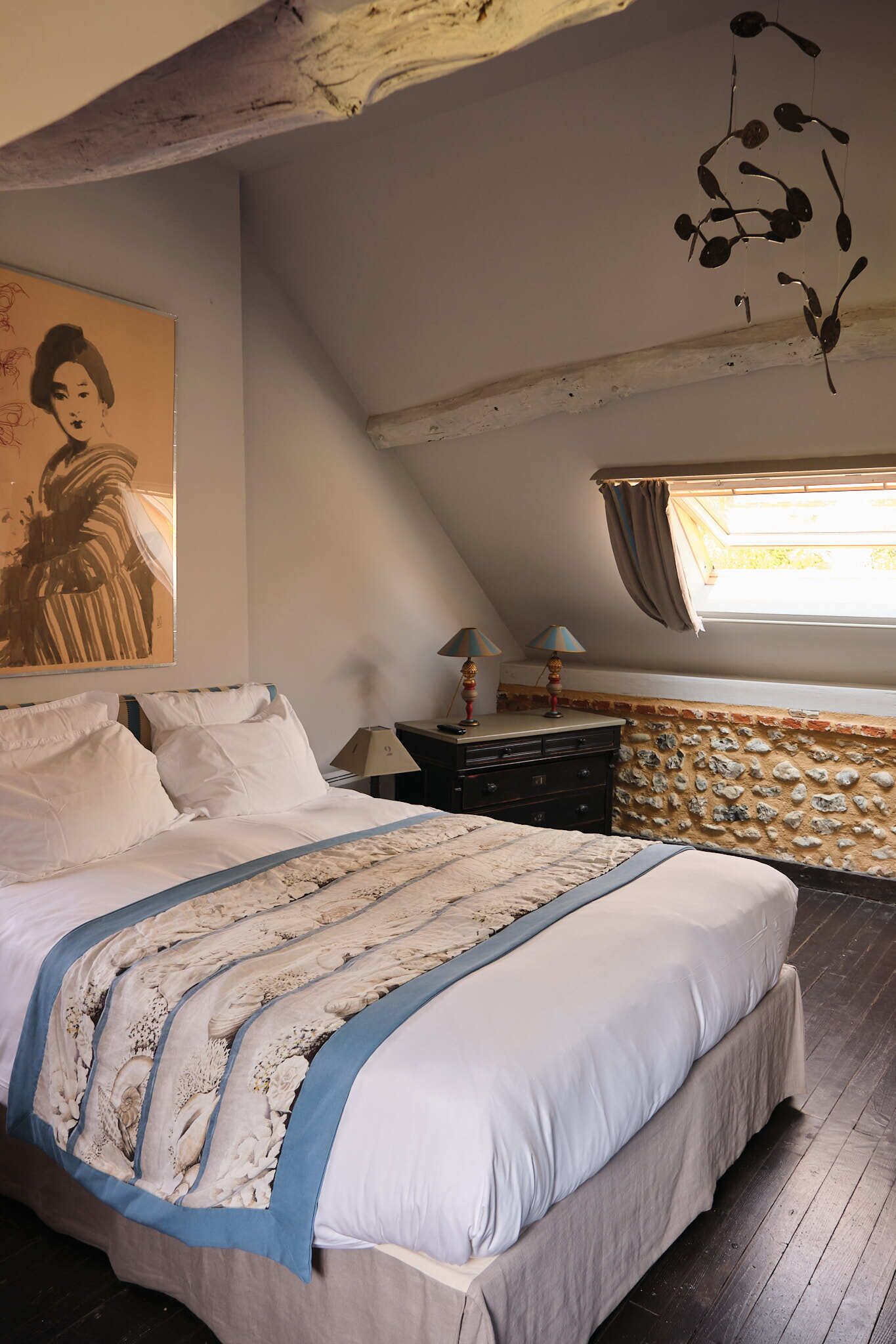 Une chambre à coucher avec un grand lit, un mur en pierre, une fenêtre avec des rideaux et un tableau accroché au mur.