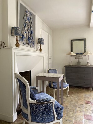 A room with a white fireplace, blue patterned chairs, a small table, and a dark dresser with a mirror. - La Maison D'aline (Pennedepie)