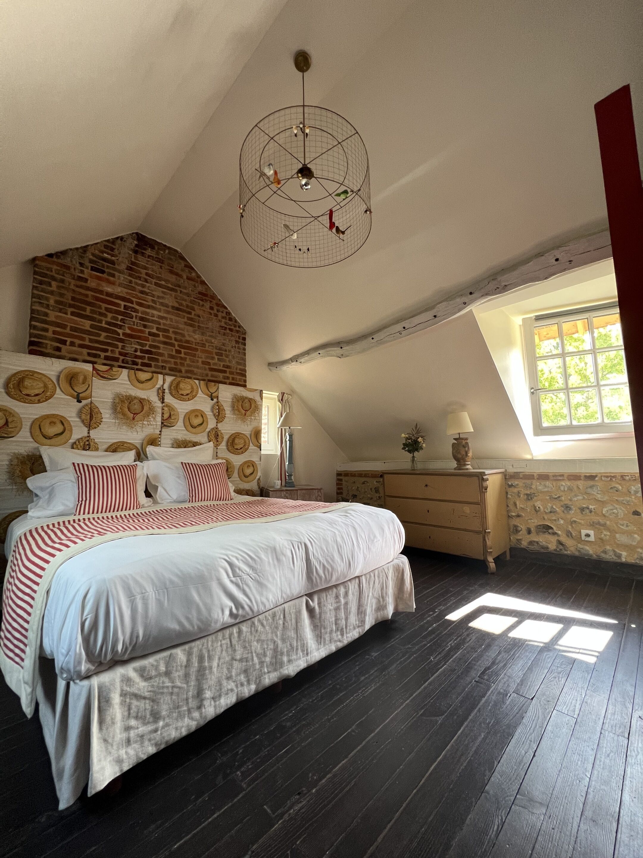 Een slaapkamer met een groot bed, een houten dressoir, een hanglamp en een bakstenen muur.