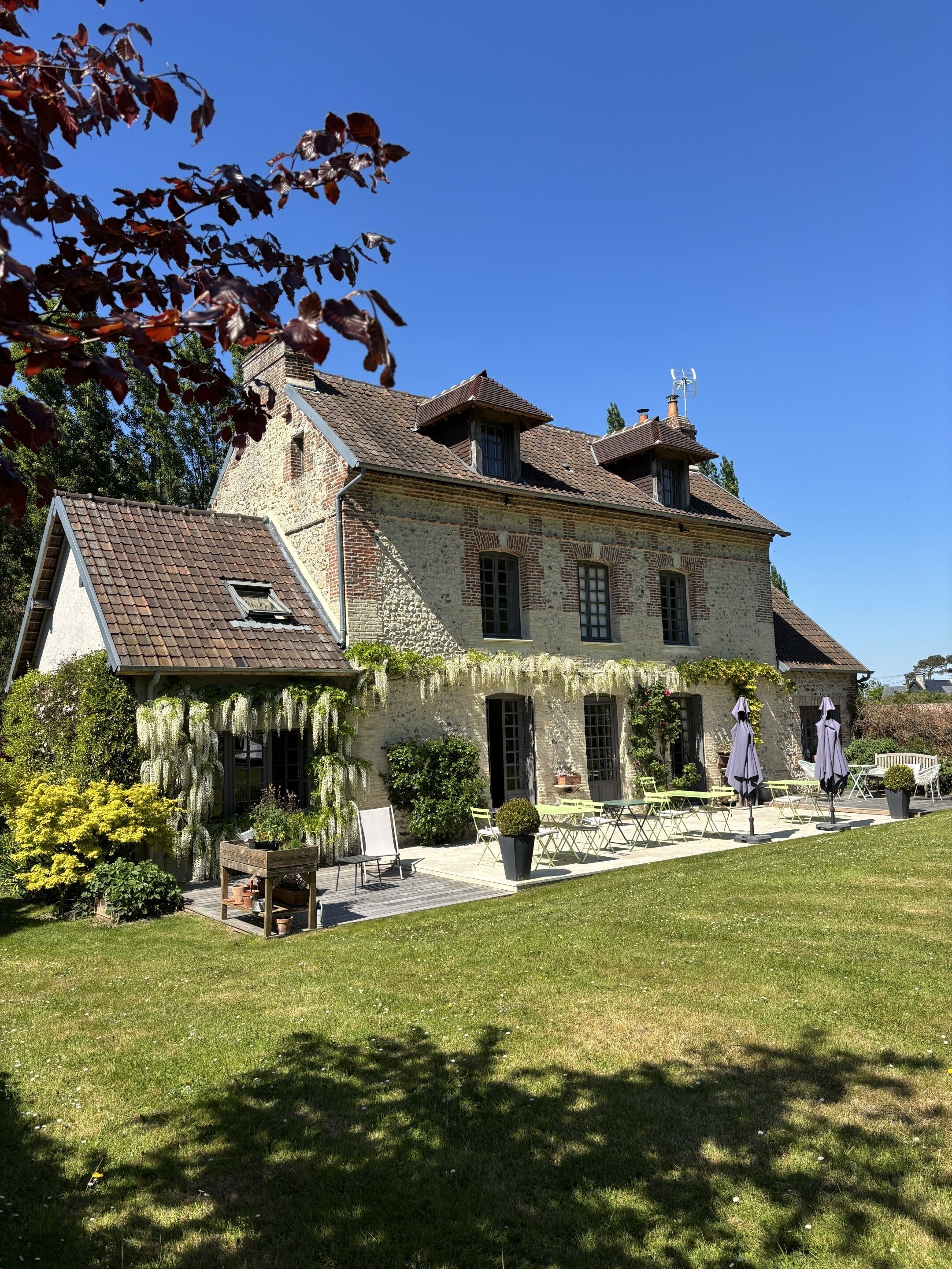 A stone building with a tiled roof, a covered patio with outdoor seating, and a well-maintained lawn.