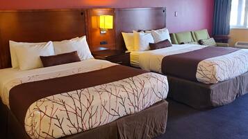 Two double beds with headboards, a nightstand, a lamp, a green chair, and a window with curtains.