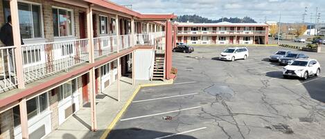 A motel with multiple floors, a parking lot with several cars, and a view of a hilly landscape in the background.