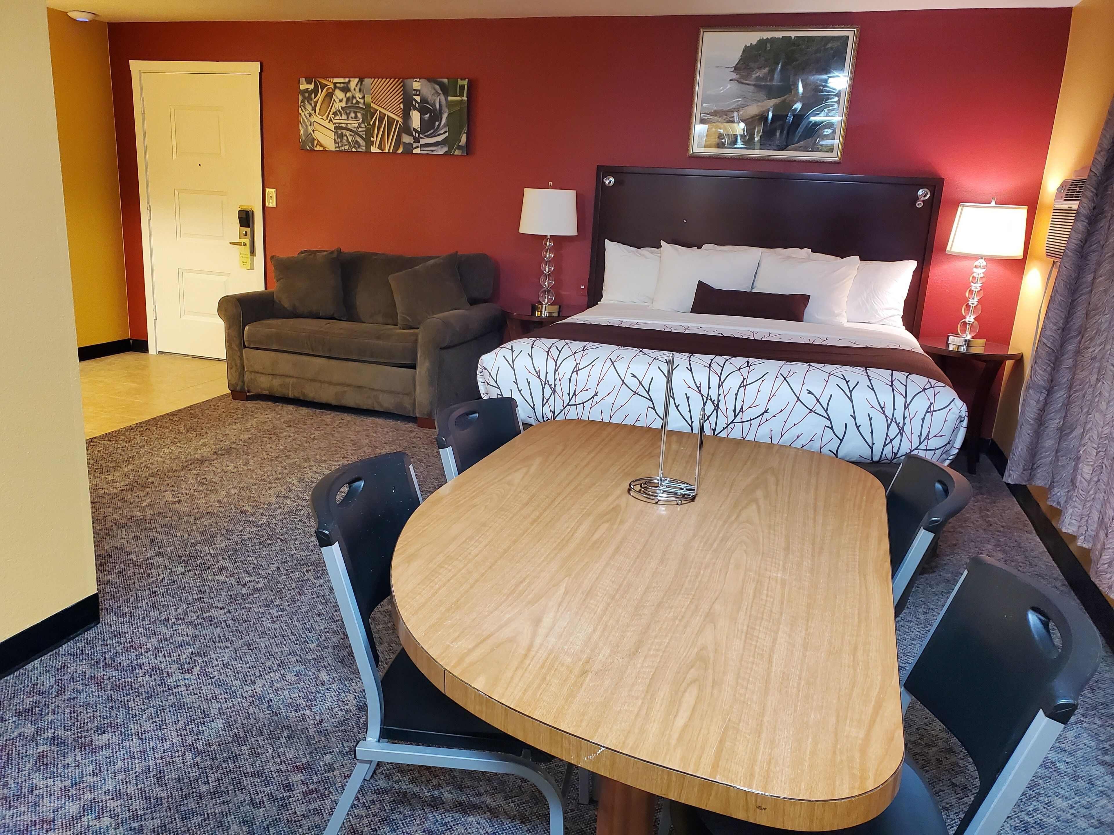 A hotel room with a bed, a sofa, a dining table, and chairs.