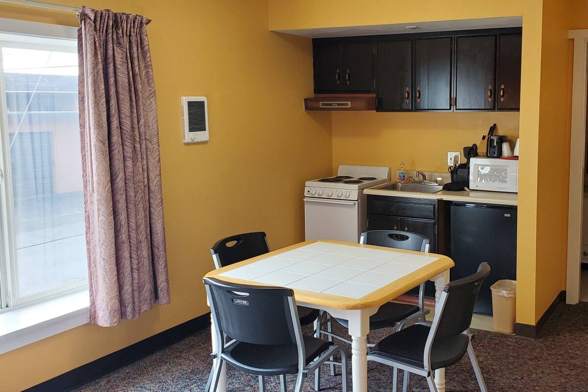 A compact kitchen with a stove, microwave, and cabinets, a dining table with chairs, and a window with curtains.