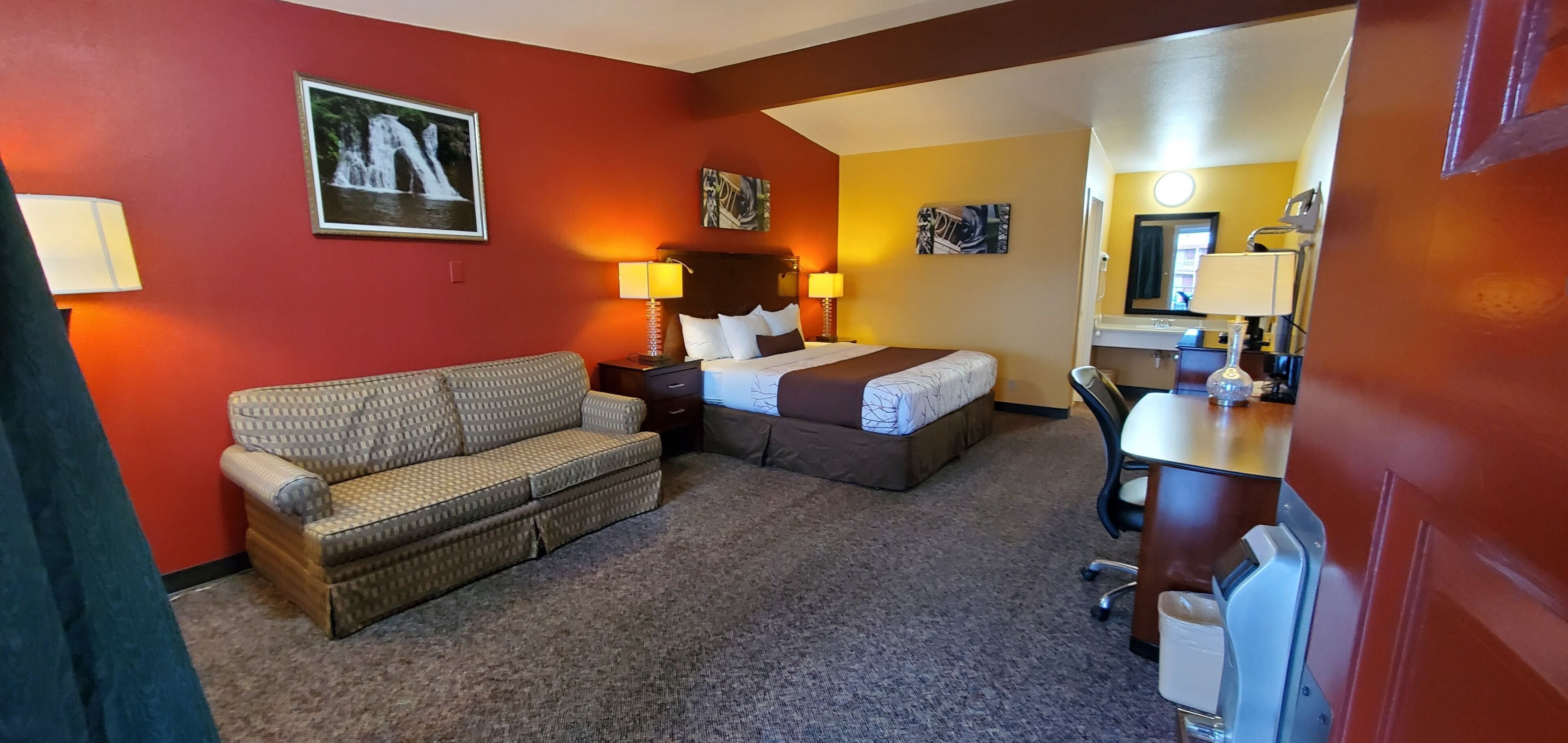 A hotel room with a bed, a sofa, a desk, and a mirror.