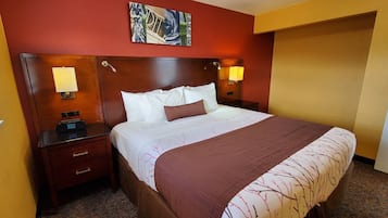 Habitación de hotel con una cama grande, dos lámparas de noche, una mesita de noche, un cuadro en la pared y una puerta.