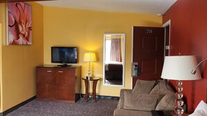 Habitación de hotel con televisor, tabla de planchar y sofá.