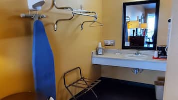 A compact hotel room with a single bed, a small table, a chair, a desk, a mirror, and a bathroom with a sink and toilet.