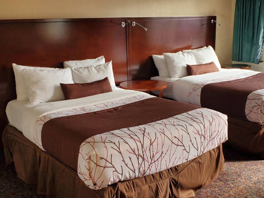 A hotel room with two beds, a small round table, and a view of the street through a window.