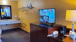 Habitación de hotel con cama, escritorio con lámpara, televisor, teléfono y cafetera.