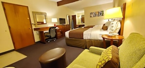 Una habitación de hotel con cama, escritorio, silla, sofá, lámpara y televisor.