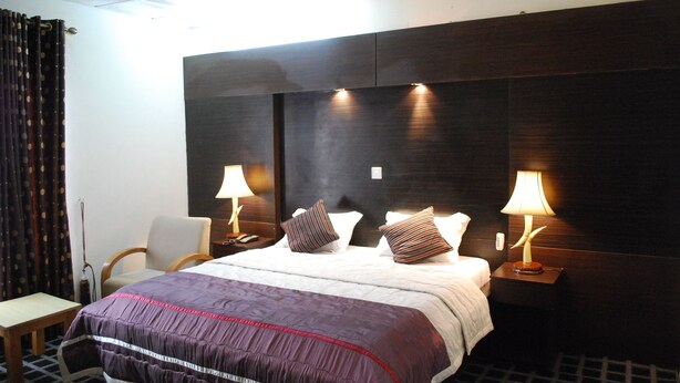Une chambre d’hôtel avec un grand lit, deux tables de chevet avec des lampes, une chaise et un rideau.