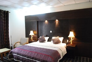 Une chambre d’hôtel avec un grand lit, deux tables de chevet avec des lampes, une chaise et un rideau.