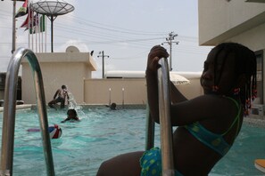 A swimming pool with metal ladders, a volleyball, and a person in the water. - Citilodge Hotel Lagos (Lekki)