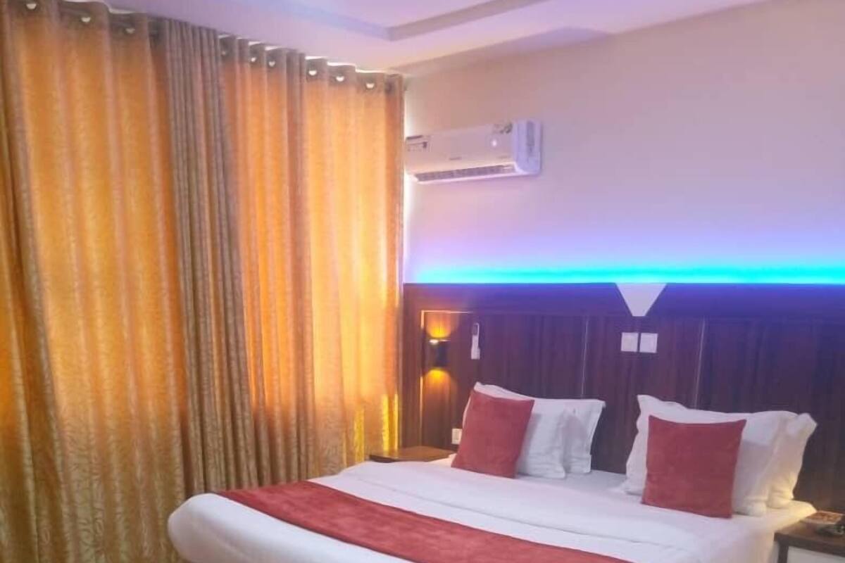 A hotel room with a large bed, a nightstand, an air conditioning unit, and a curtain.